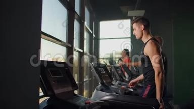 男人在健身室里踩着跑步机走路。 一群人走在跑步机上，靠近一个大的全景窗口。 开始